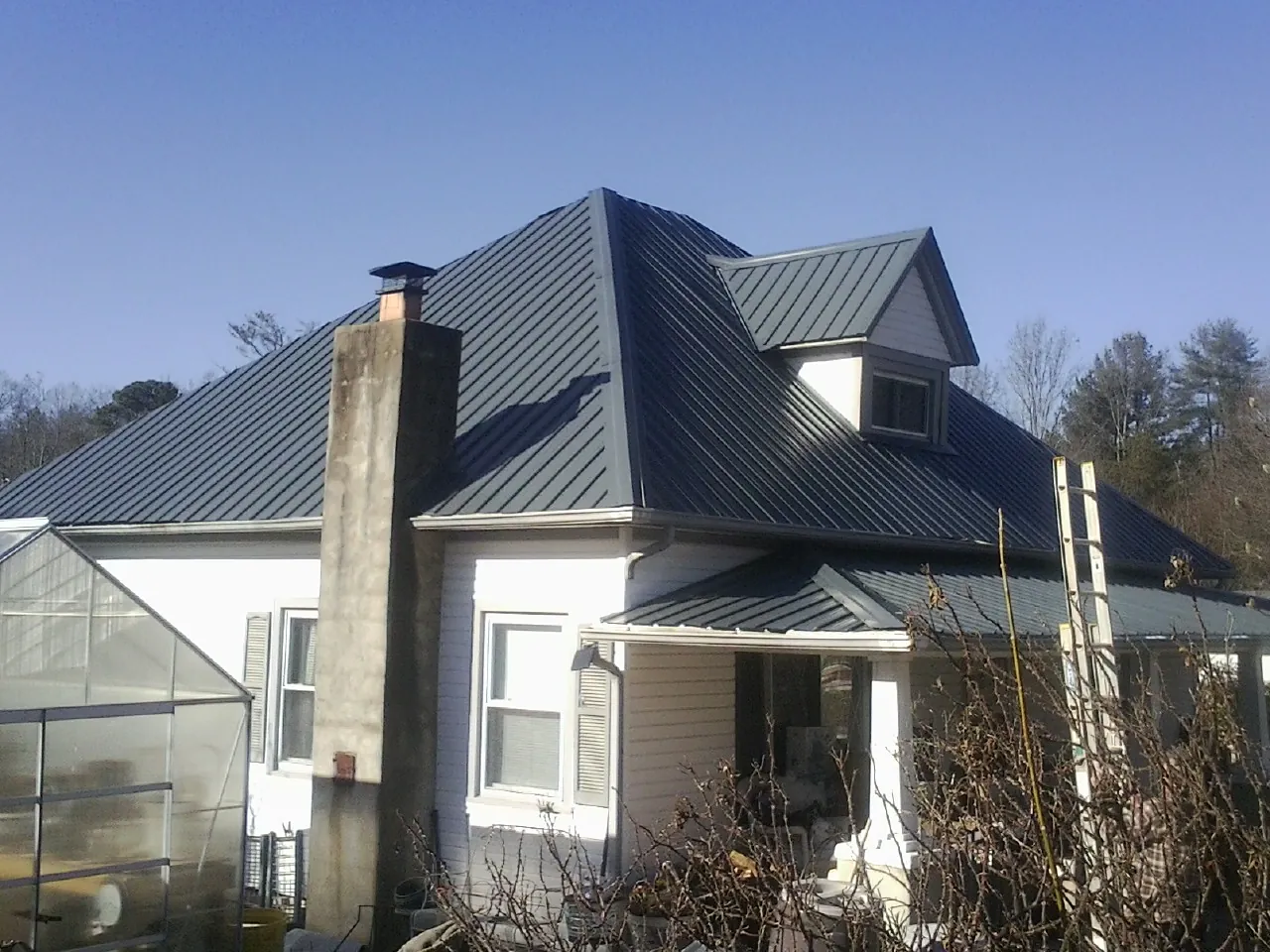 Dark blue standing seam metal roof on a white farmhouse with dormer — Slate & Tile Roof Repair by Roofing Brothers in Lansford