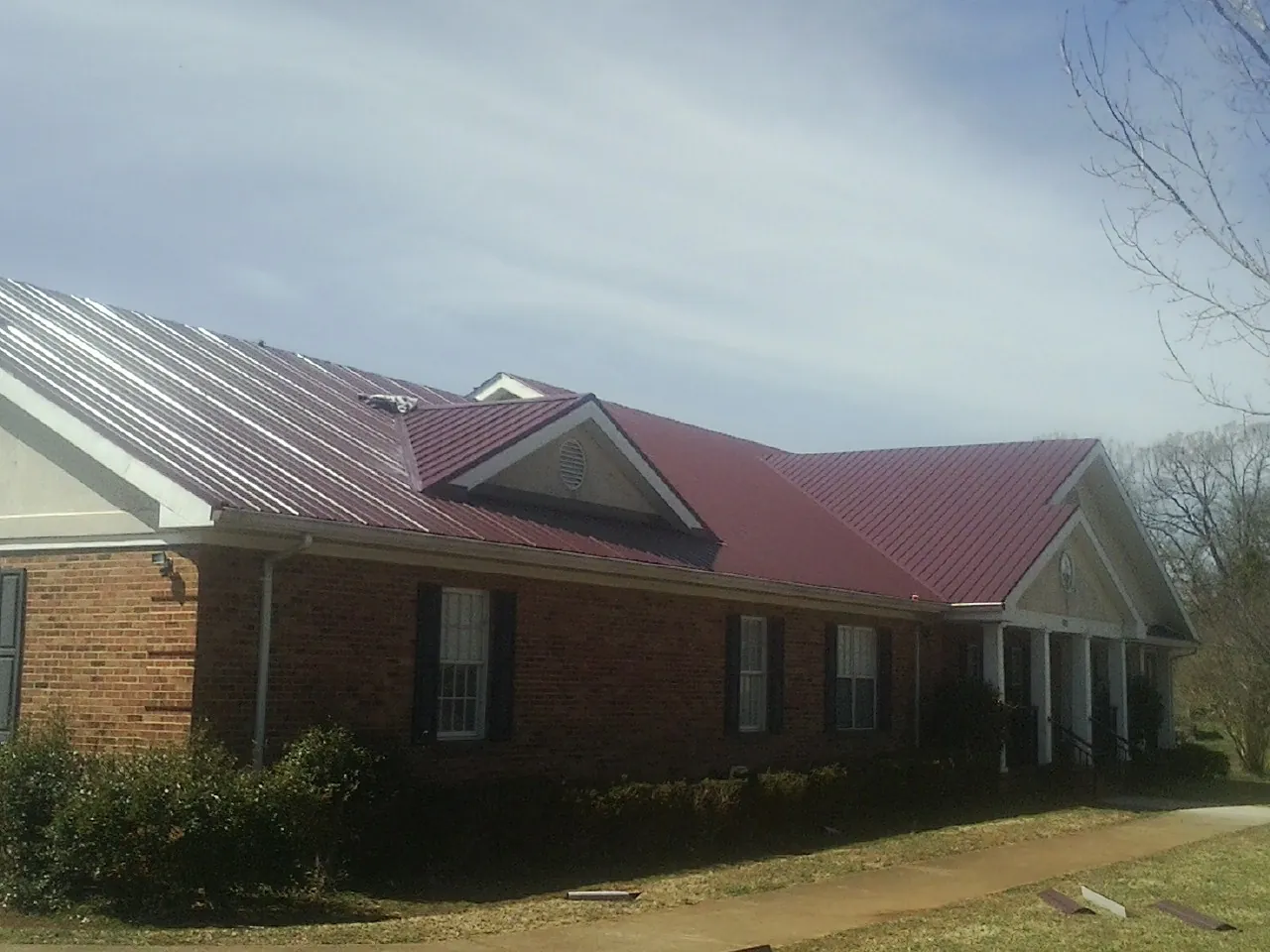 Red metal roof with gabled entries on a long brick building, from a Hail Damage Roof Repair job in Lansford