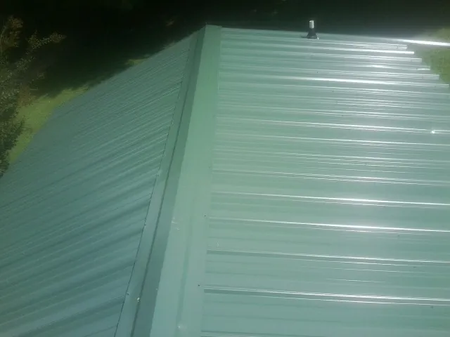 New green metal panels meeting at the ridge of a roof — Flat Roof Repair work by our crew in Lansford