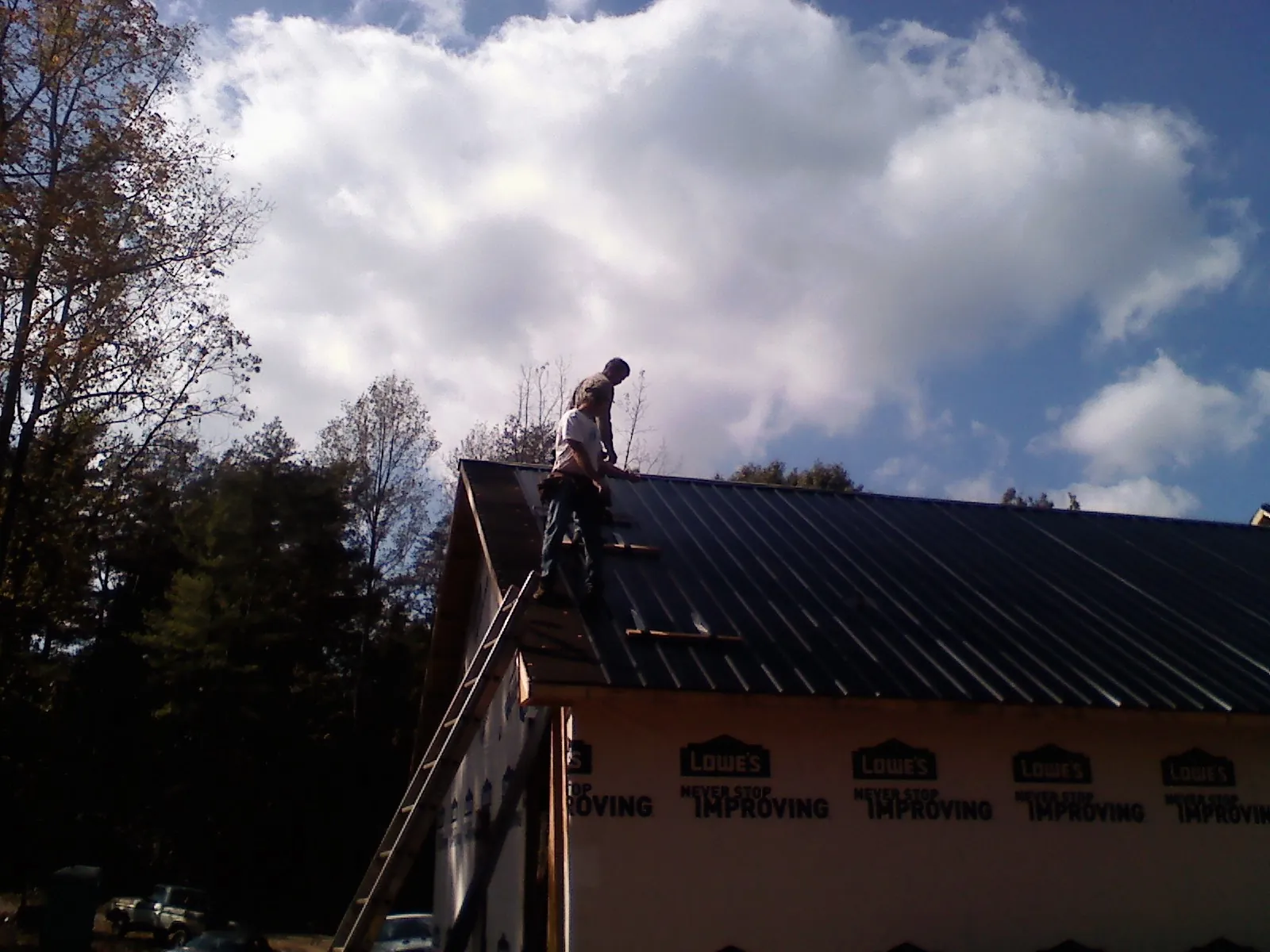 Roofer fastening dark metal panels high against a cloudy sky, from a Roof Inspection job in Lansford