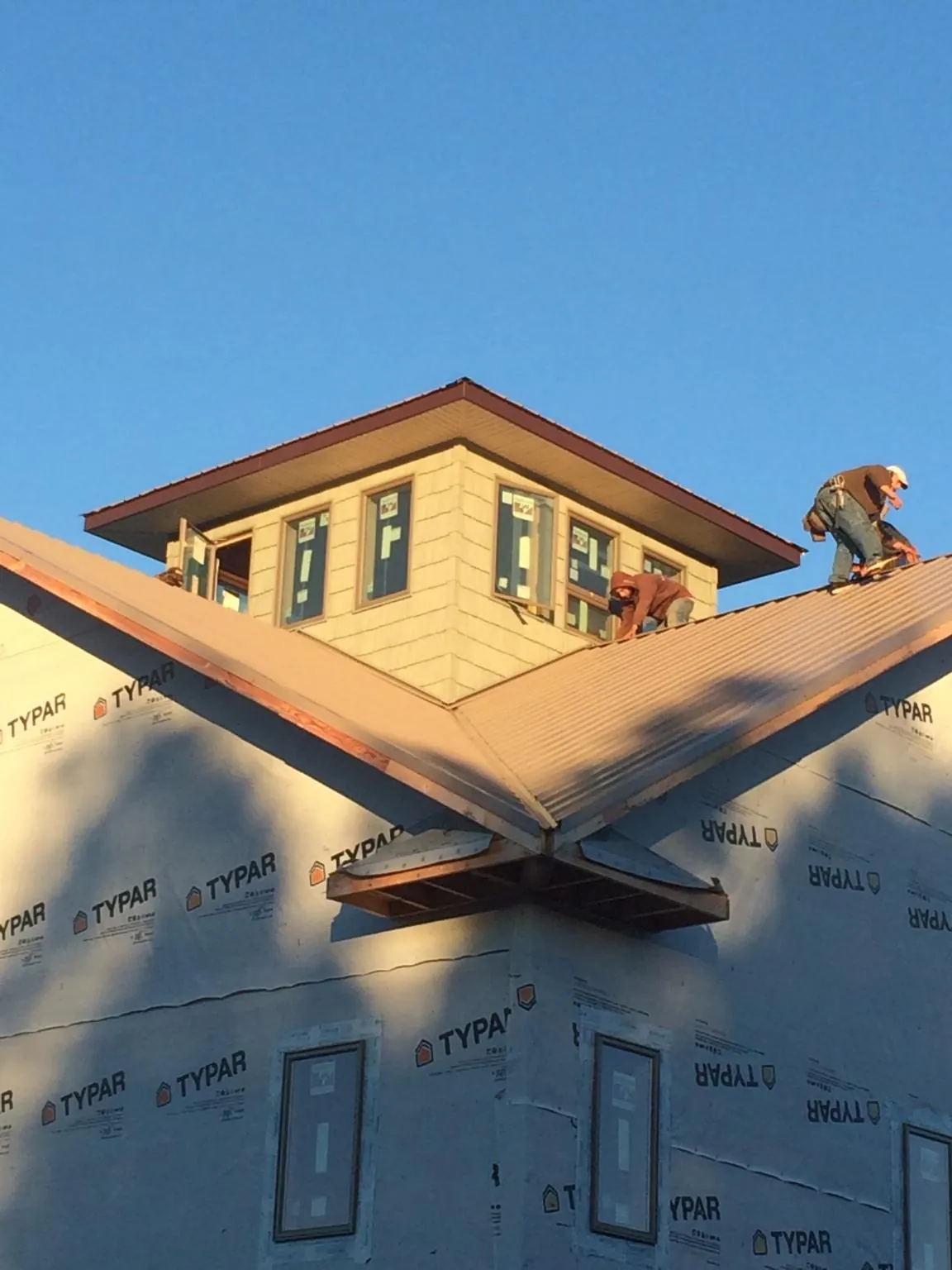 Roofers working around a rooftop cupola on a new metal roof at sunset in Lansford
